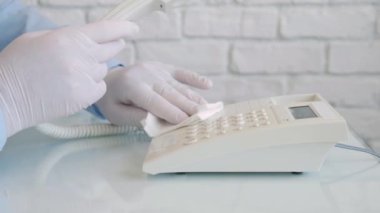 Ellerinde koruma eldivenleri olan, sprey ve ıslak mendil kullanarak telefonu temizleyen ve dezenfekte eden bir adamla Yavaş Hareket