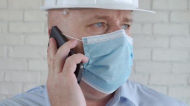 Güvenli Miğferli Mühendis ve yüzünde bir koruma maskesi Cep telefonuyla konuşuyor