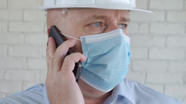 Mérnök biztonsági sisakkal és védőmaszkkal az arcán beszél a mobiltelefonhoz. — Stock videók