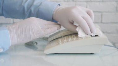 Ellerinde koruma eldivenleri olan, sprey ve ıslak mendil kullanarak telefonu temizleyen ve dezenfekte eden bir adamla Yavaş Hareket