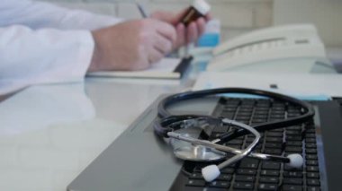 Slow Motion Doctor bazı ilaçlara bakıyor ve bir tedavi öneriyor, doktor hastane danışma odasında tıbbi bir tarif yazıyor.