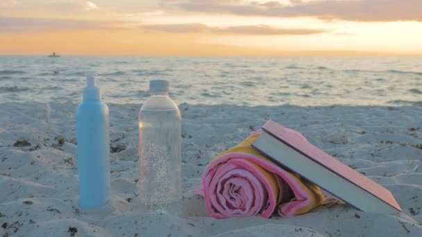 Acessórios de praia, uma garrafa de água, toalha, óculos de sol, protetor solar e um livro — Vídeo de Stock