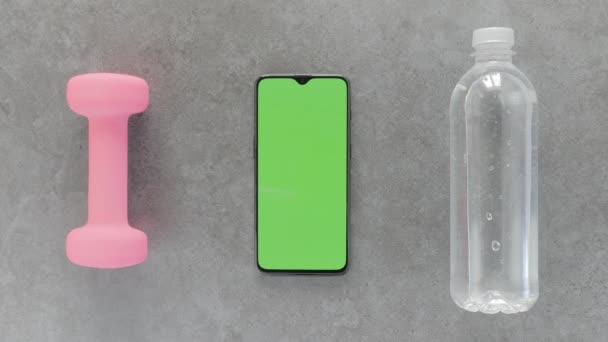 Pantalla verde: un Smartphone, una botella de agua y una mancuerna sobre una mesa — Vídeos de Stock