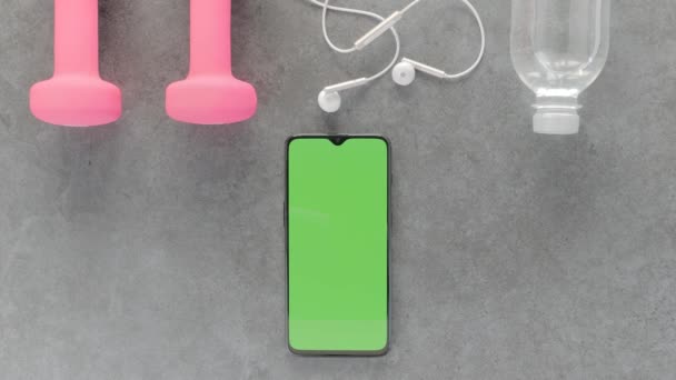 Groen scherm-een smartphone, waterfles, koptelefoon en dumbbells op een tafel — Stockvideo
