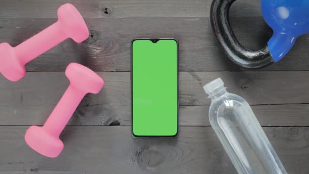 Zielony ekran-smartfon, butelka wody i hantle na stole — Wideo stockowe