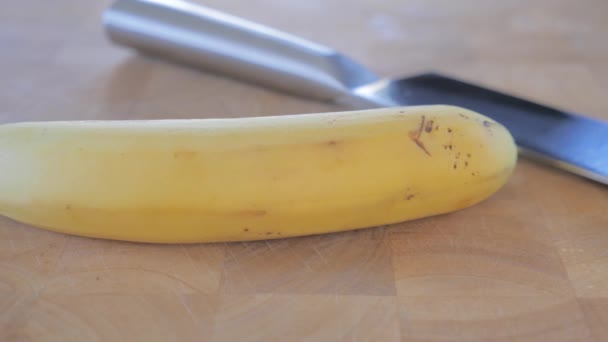 Primer plano de un plátano y un cuchillo en la tabla de cortar . — Vídeos de Stock