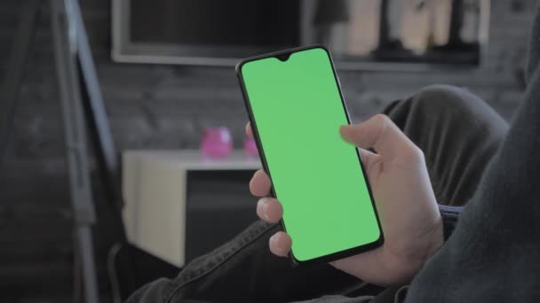 Pantalla verde: un hombre en la sala de estar mirando un teléfono inteligente y deslizando — Vídeos de Stock