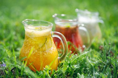 Yeşil G 'nin üzerinde farklı renklerde limonata bulunan cam sürahiler.