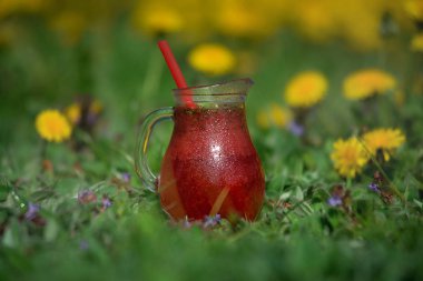 Cam sürahide kırmızı limonata ve üzerinde pipet var.