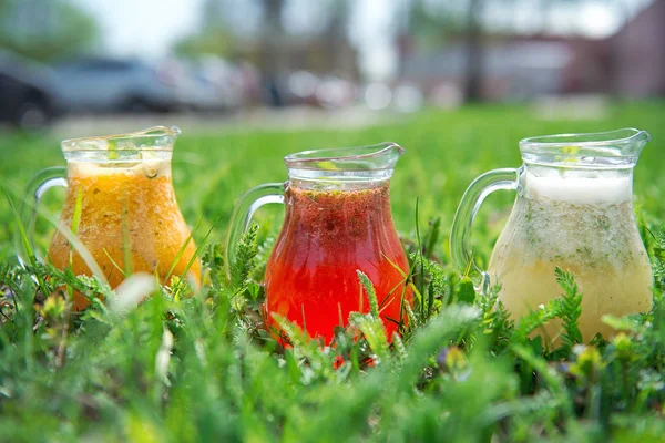 Yeşil G 'nin üzerinde farklı renklerde limonata bulunan cam sürahiler.