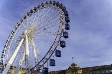 Mavi yolcu kamaralı dev dönme dolap. Açık mavi gökyüzü üzerinde. Avrupa mimarisi olan tarihi bir binanın yakınında..