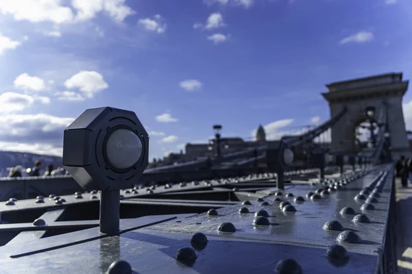 Macaristan, Budapeşte 'deki Budapeşte Kalesi' nin bulanık arka planına sahip Szechenyi Zinciri Köprüsü 'nde metalik perçin ve lambaların yakın çekimi.