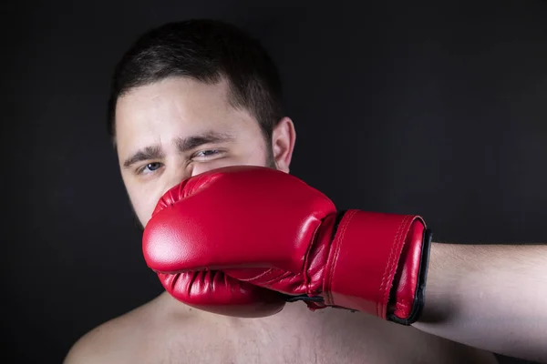 Boxer in red gloves for boxing strikes the opponent to the man. A man with beard is beaten in the face with his fist. Pain from the impact.