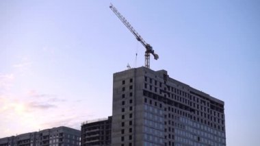 Bir inşaat vinç kargo taşımaktadır. Günbatımı City. Çok katlı bina inşaatı.