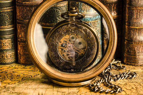 Antique clock on the background of a magnifying glass and books.