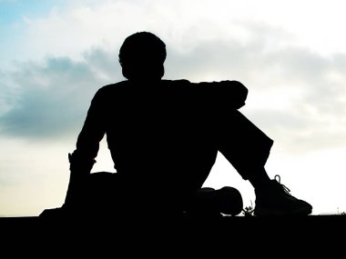 Duvar oturan genç adam silüeti, duvarda oturan genç adam