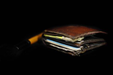 İçinde banknotlar, kredi kartları ve siyah arka planda izole edilmiş makyaj fırçası bulunan yeni gerçek deri cüzdanın üst görüntüsü.