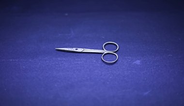 Mavi saplı, yumuşak arka planlı saç kesimleri için metalik makas.