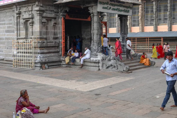 THIRUVANNAMALAI, INDIEN - 24. Dezember 2019: Eine ältere Frau sitzt vor einem Tempel, eine Gruppe von Menschen sitzt in der Nähe des Eingangs zum Hindutempel — Stockfoto