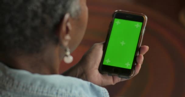 Oudere zwarte vrouw op zoek naar haar slimme telefoon met een chroma key greenscreen — Stockvideo