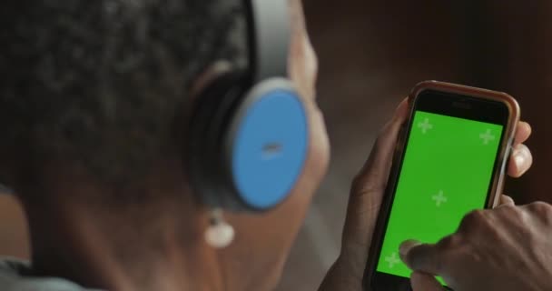 Пожилая пожилая черная женщина выбирает музыку из своего смартфона с зеленым экраном — стоковое видео