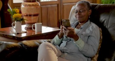 Mutlu gülümseyen yaşlı siyah kadın akıllı telefonunu evde kullanma