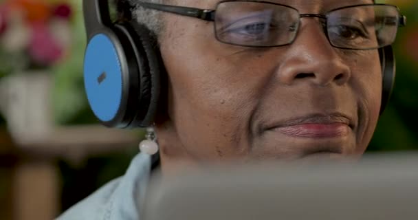 Ανώτερος μαύρη γυναίκα απολαμβάνοντας μουσική με τα ακουστικά ενώ χρησιμοποιείτε μια ψηφιακή οθόνη — Αρχείο Βίντεο
