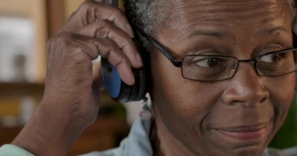 Senior black woman putting on headphones and listening to music — Stock Video