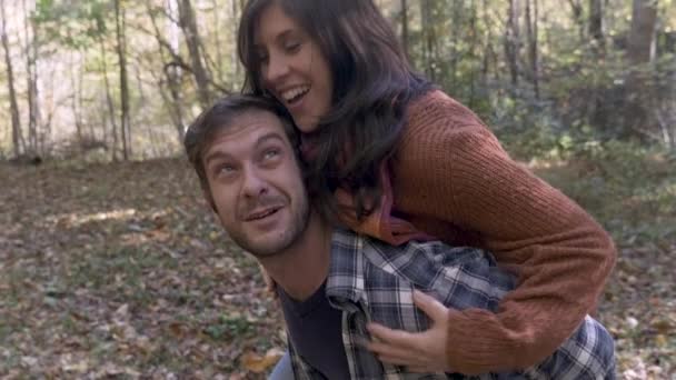 Улыбающийся мужчина с привлекательной женщиной на спине во время прогулки по лесу — стоковое видео