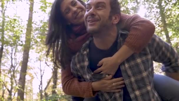 Boldog egészséges ember kezében egy fiatal nőt a hátán a szabadban az erdőben — Stock videók