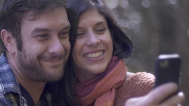 Мужчина делает селфи со смартфоном, целуя женщину в щеку — стоковое видео