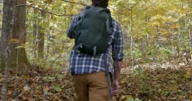 Kamera ormanda yürüyüş veya yürüyüş bir sırt çantası ile genç bir adam takip