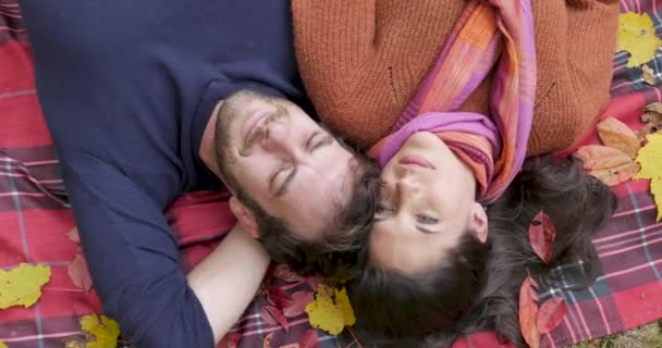 Jovem casal sorridente feliz deitado em um cobertor com folhas de queda - tiro aéreo — Vídeo de Stock