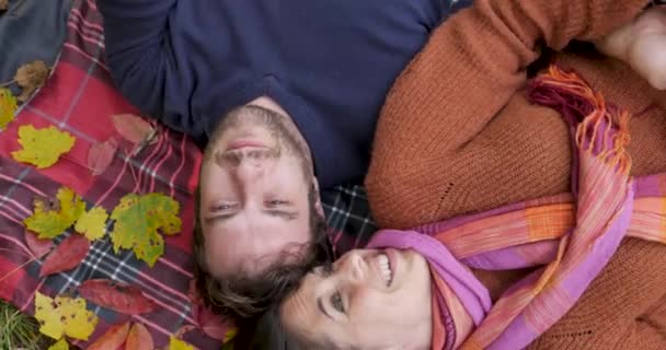 Jong paar in de liefde liggend op een deken met herfstbladeren-overhead shot — Stockvideo