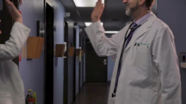 Два счастливых доктора дают пять и показывают друг другу большие пальцы, отмечая — стоковое видео