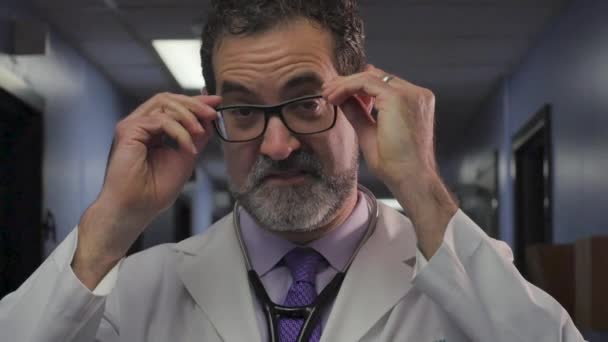 Красивий чоловік-лікар знімає окуляри, стоячи в лікарняному коридорі — стокове відео