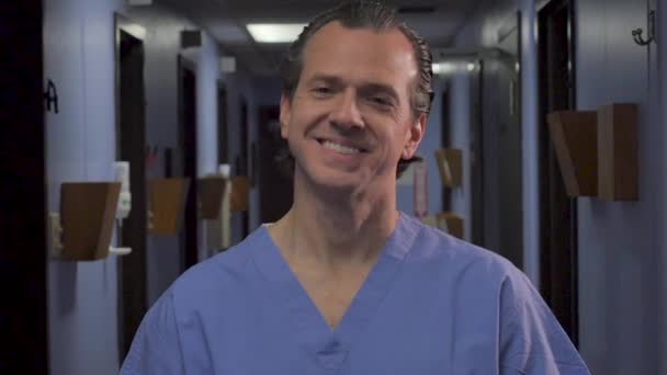 Hombre vistiendo uniformes azules sonriendo y mirando a la cámara en una clínica médica — Vídeo de stock