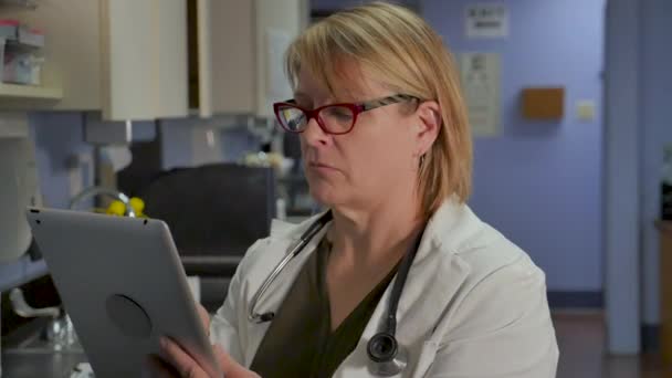 Ärztin gibt in einem Krankenhaus oder einer Arztpraxis Informationen auf einem Tablet ein — Stockvideo
