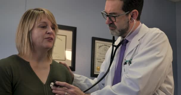 Male doctor using a stethoscope on a female patient during a medical exam — Stock Video