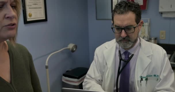 Doktor bir kadın hasta görüşmeleri olarak bir bilgisayara notlar yazmaya odaklanarak — Stok video