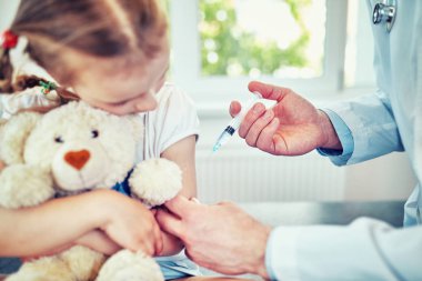 Doktor Pediyatrist tatlı bir kıza aşı enjekte ediyor.