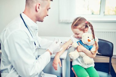 Doktor Pediyatrist tatlı bir kıza aşı enjekte ediyor.