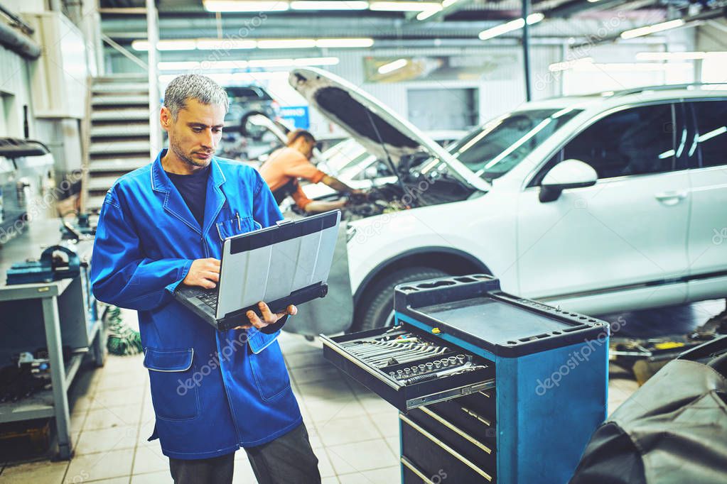 mechanic man with automotive diagnostic scanner and clipboard checking car system at workshop