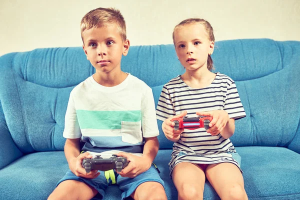Children emotionally play a video game while sitting on the couc