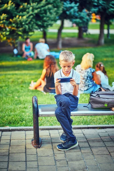 Um jovem senta-se em um parque e usa o telefone — Fotografia de Stock