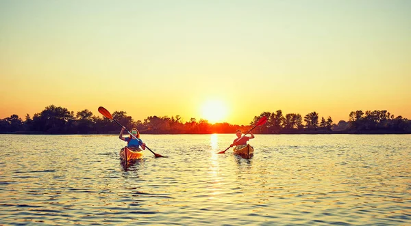 La gente kayak durante la puesta del sol en el fondo. Diviértete en tu f — Foto de Stock