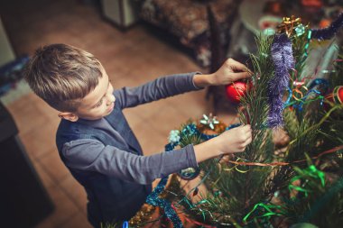 Noel arifesinde bir çocuk evde bir Noel ağacı süsler.