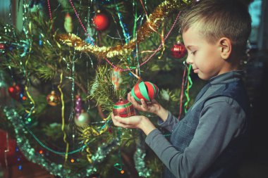 Noel arifesinde bir çocuk evde bir Noel ağacı süsler.