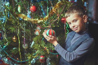 Noel arifesinde bir çocuk evde bir Noel ağacı süsler.