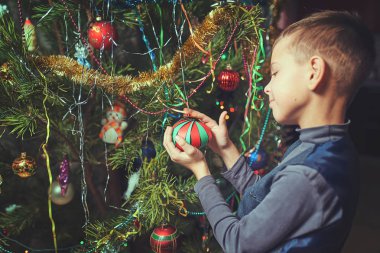 Noel arifesinde bir çocuk evde bir Noel ağacı süsler.